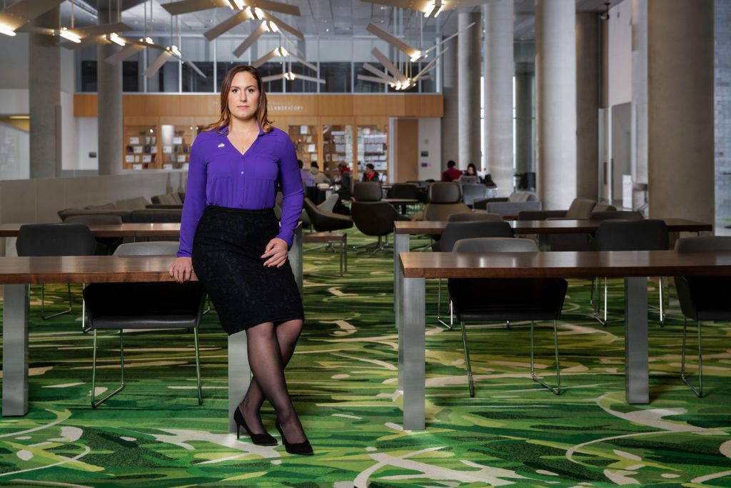 Photograph of woman, Katy Quartaro, in business clothes and seated in the library of Syracuse University