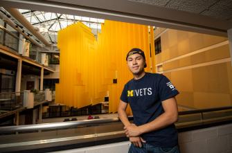 Image of University of Michigan PAVE Team member, Dominic Petersen, standing in front of a block M.