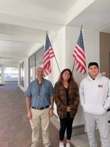 Three figures standing in front of two upright American flags