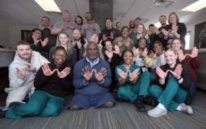 Group of people seated on the floor, each making a "W" with their hands