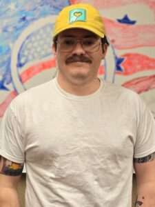Smiling man with a mustache standing in a yellow hat